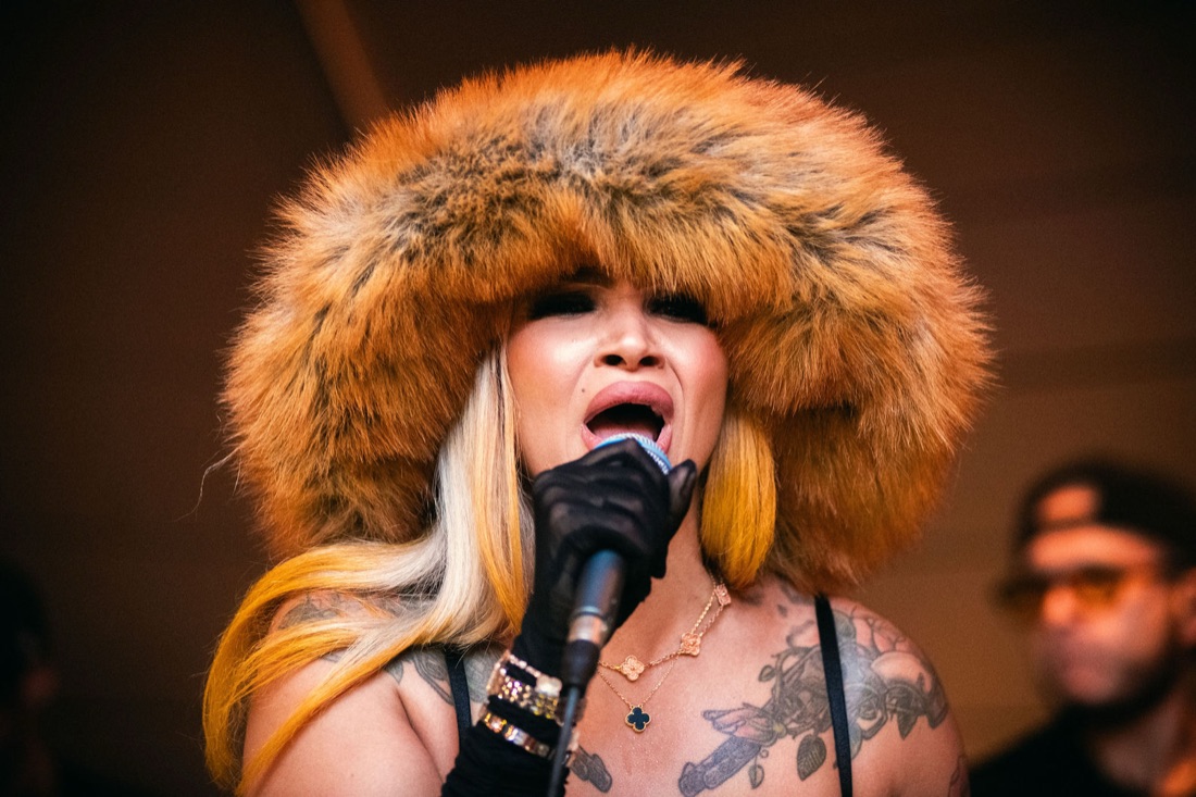 Melanie Halfkenny belting into the microphone, fur hat backlit by amber stage light — photo by Joren Photography