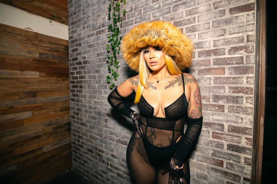 Melanie Halfkenny in fur hat against a textured brick wall, sleeve tattoos visible — photo by Joren Photography